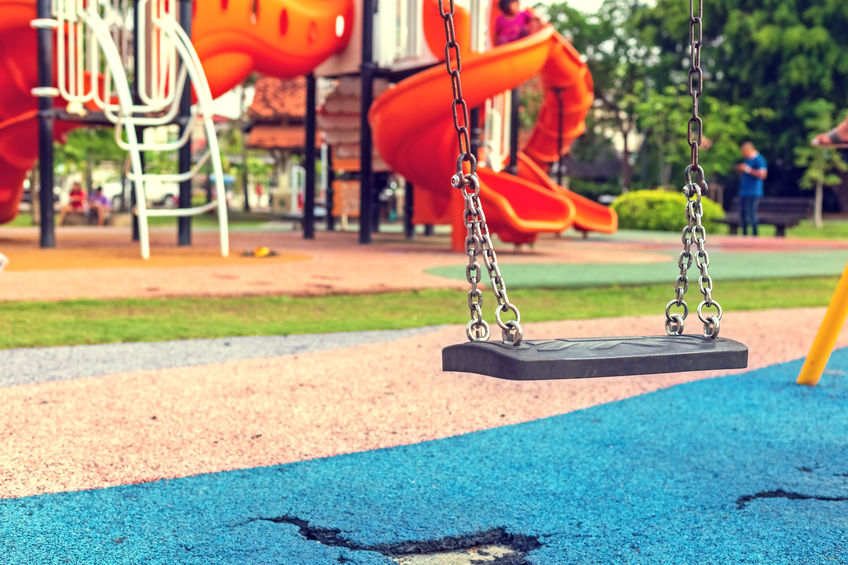 Playground swing in a park with cracked PIP rubber on ground