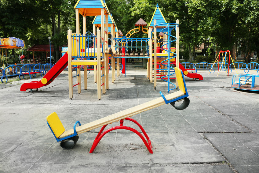 Colorful playground in public park with old, worn rubber tiles
